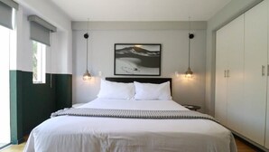 Un dormitorio moderno con una cama grande, cabecera, dos lámparas colgantes, un cuadro en la pared y un armario.