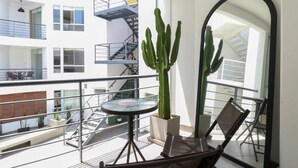 Un balcón con un cactus, una mesa redonda de vidrio y dos sillas.