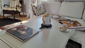 Una sala de estar acogedora con un sofá blanco, una mesa de centro con un libro y una tetera, y una lámpara.