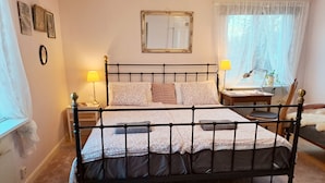 Un dormitorio con cama con dosel, una mesita de noche con lámpara, un espejo en la pared y una ventana con cortinas traslúcidas.