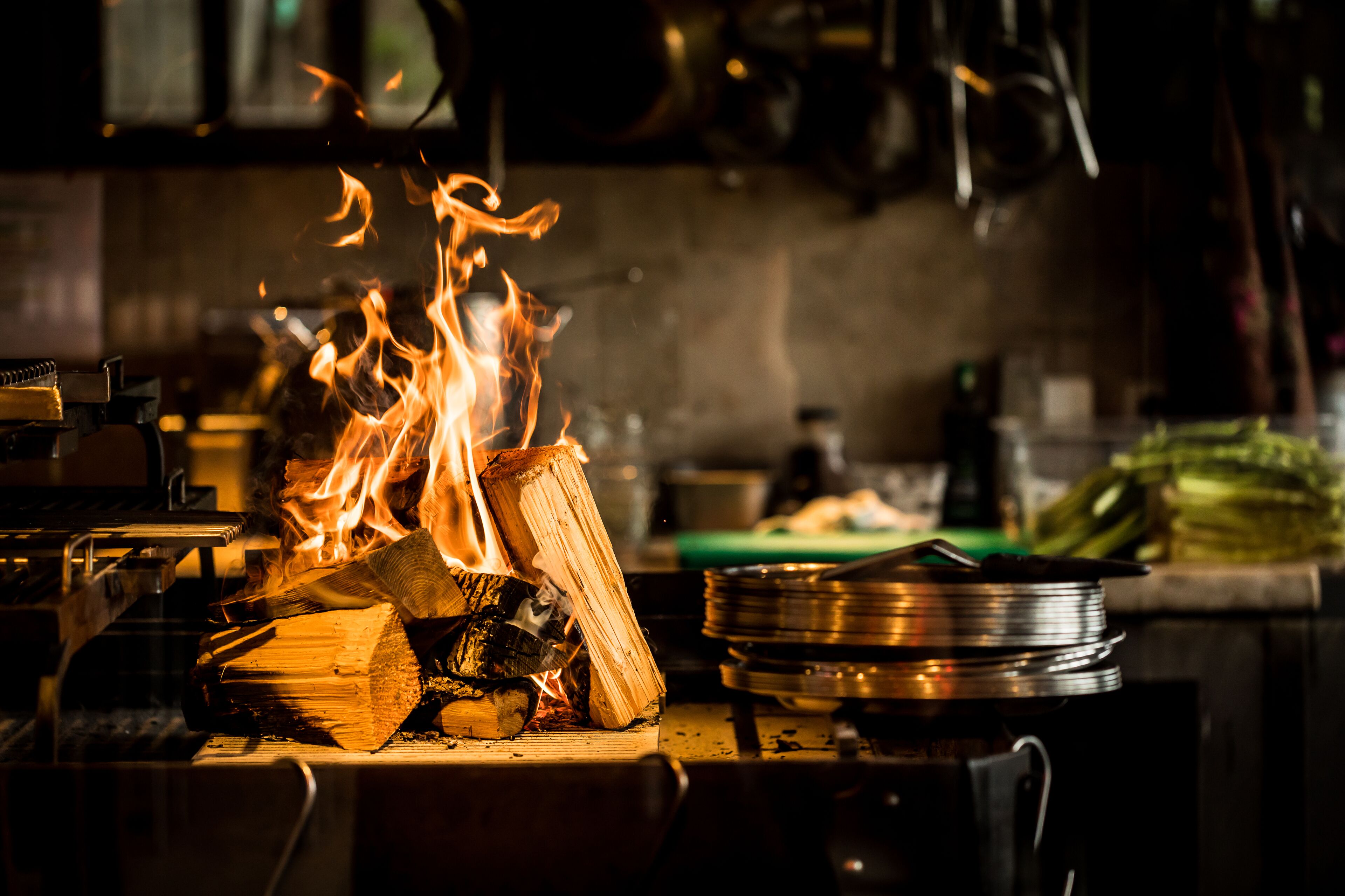 A kitchen with a wood fire burning, cooking utensils, and pots on the stove.