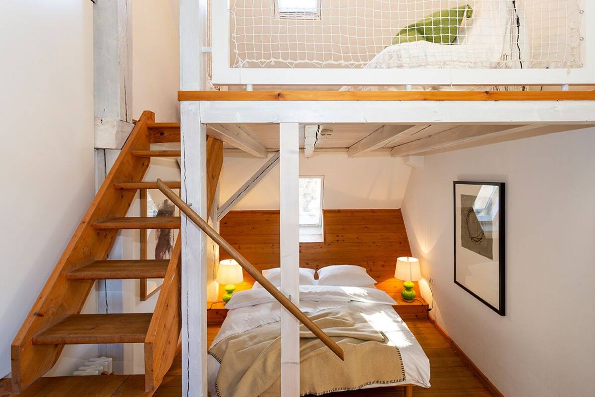 Une chambre avec un escalier en bois, un lit superposé et une table de chevet avec des lampes.