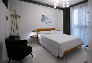 A modern bedroom with a wooden bed, a black chair, a small side table with a lamp, and a decorative wall piece.