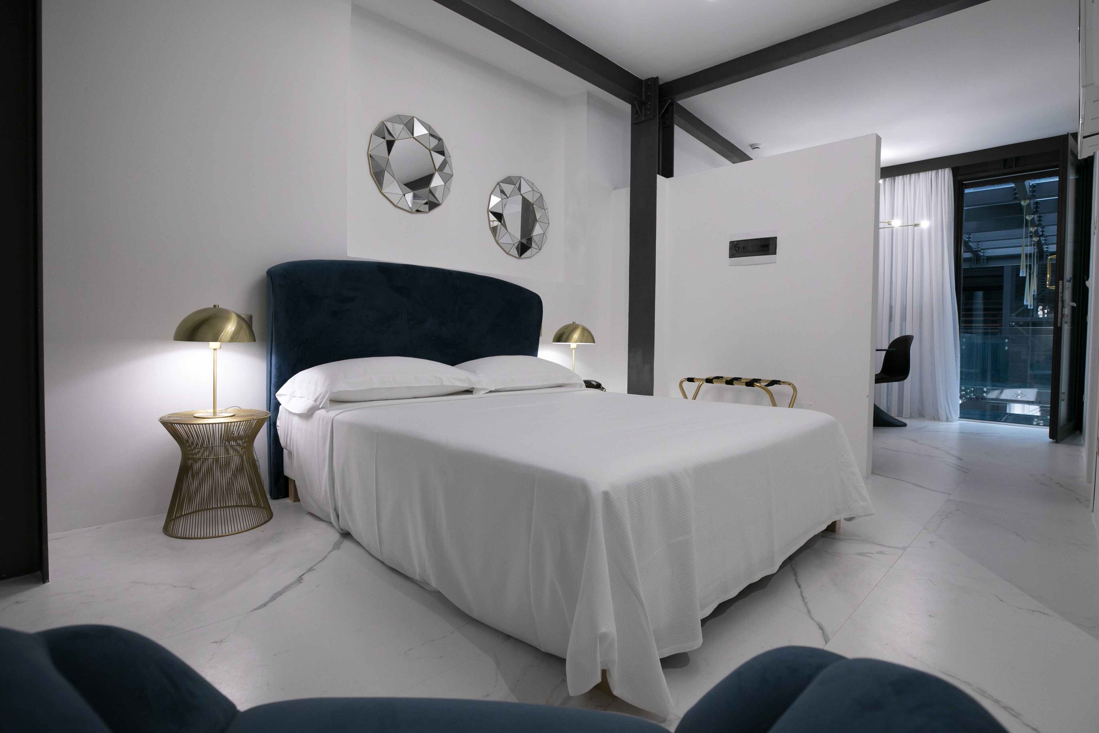 Een moderne slaapkamer met een groot bed, twee bedlampen en decoratieve spiegels aan de muur.
