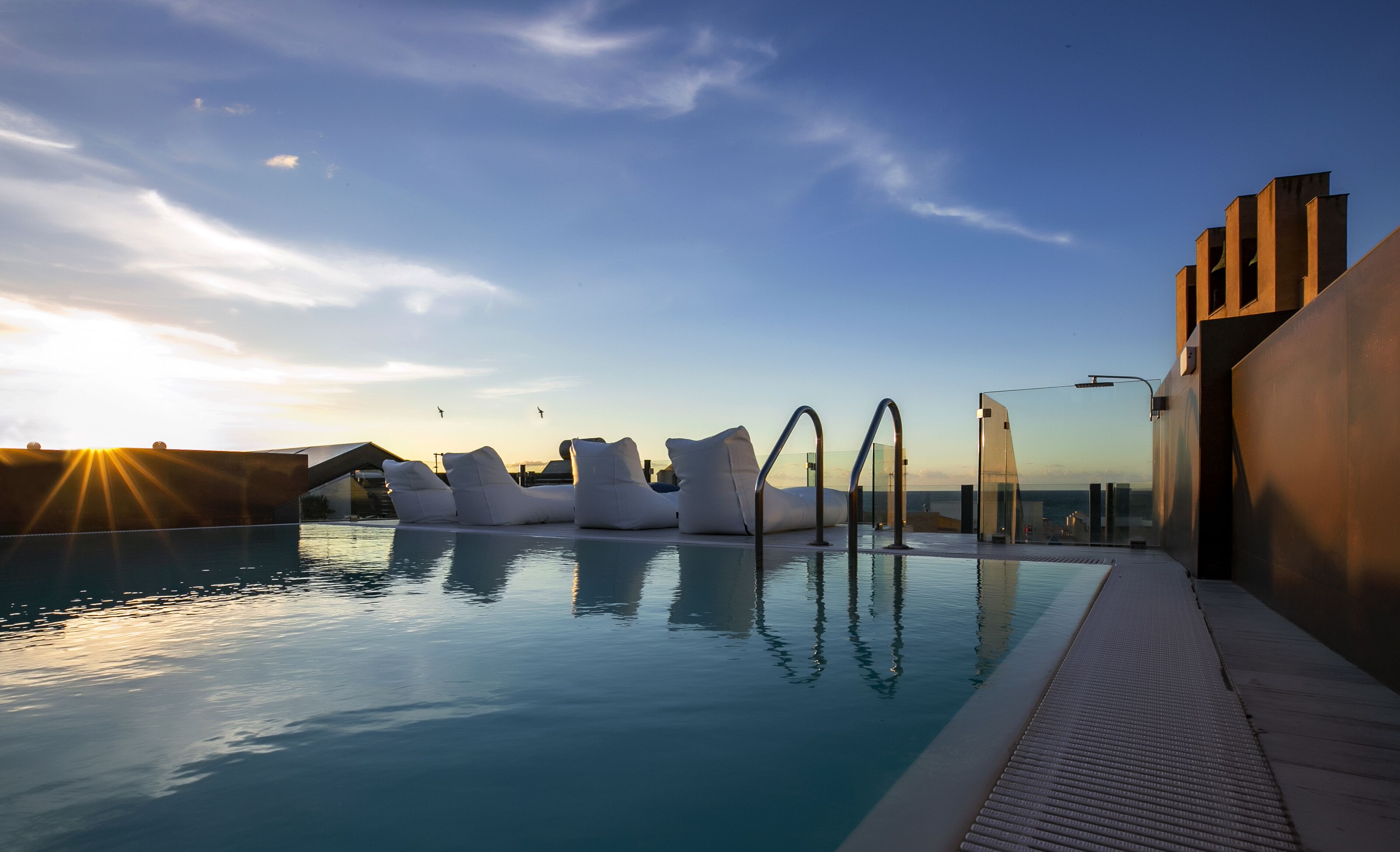 A pool with modern seating and a clear view of the sunset.
