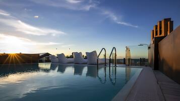 A pool with modern seating and a clear view of the sunset.