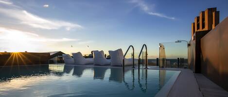 A pool with modern seating and a clear view of the sunset.