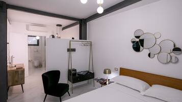 Una habitación de hotel moderna con una cama, una silla negra, una mesita de noche con una lámpara, un espejo en la pared y un estante con un televisor y otros objetos.