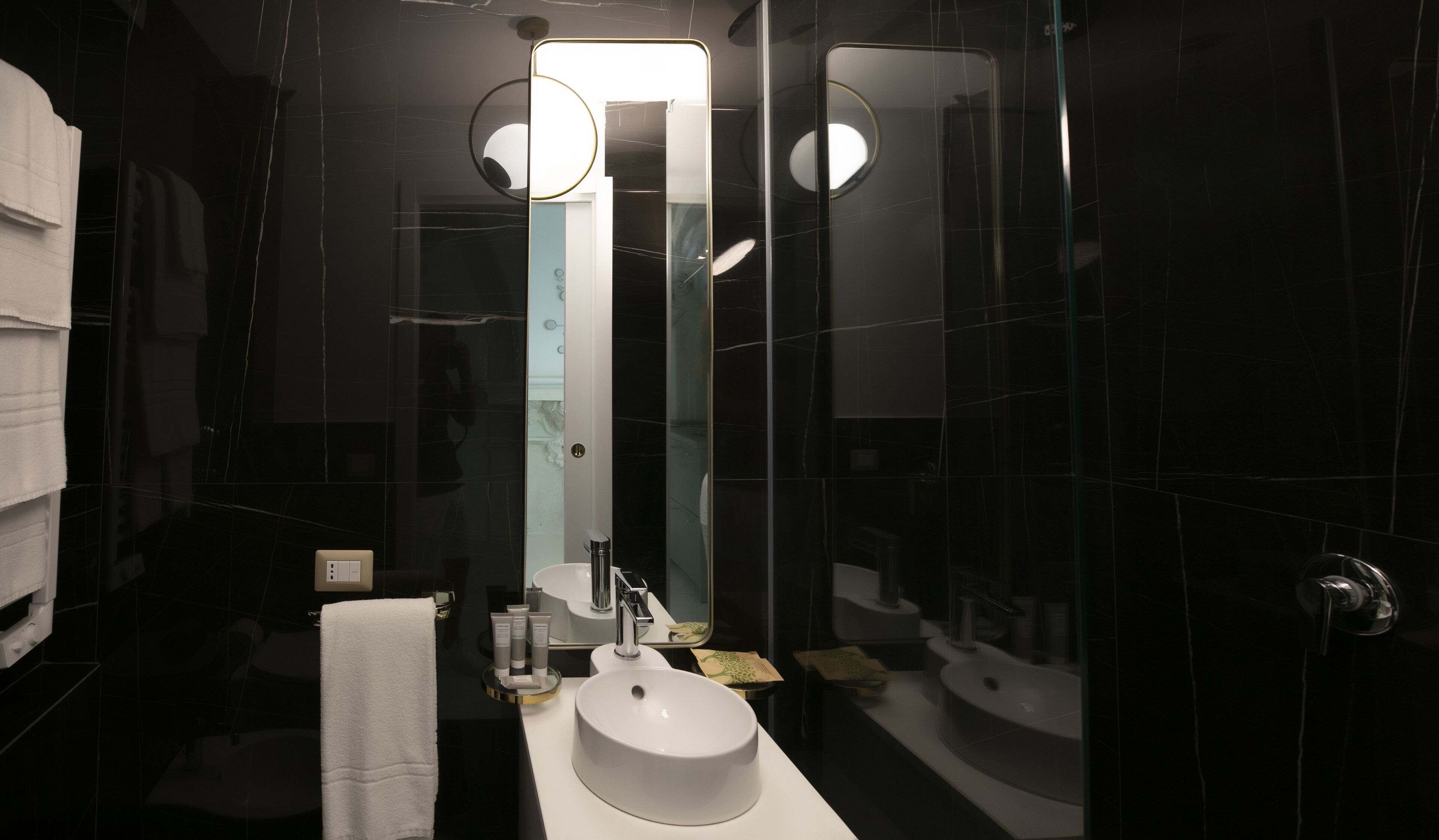 Un baño moderno con un espejo grande, un lavamanos blanco y una zona de ducha con cerramiento de vidrio.