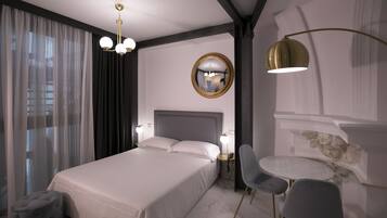 A modern hotel room with a large bed, bedside tables with lamps, a round mirror, and a small round table with chairs.