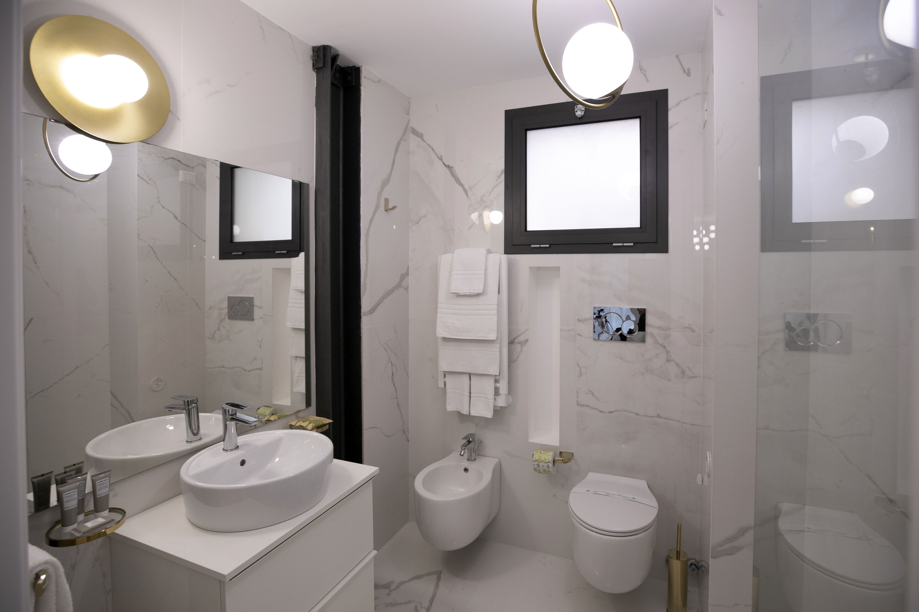 A modern bathroom with two sinks, a bidet, a toilet, and a large mirror with a television above it.