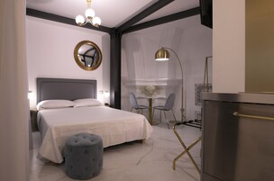 A modern bedroom with a bed, bedside tables, a round mirror, a desk with chairs, and a refrigerator.