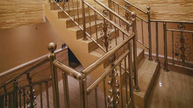 A grand staircase with ornate metal railings and a marble wall. - Ubiq Suites and Apartments (Abuja)
