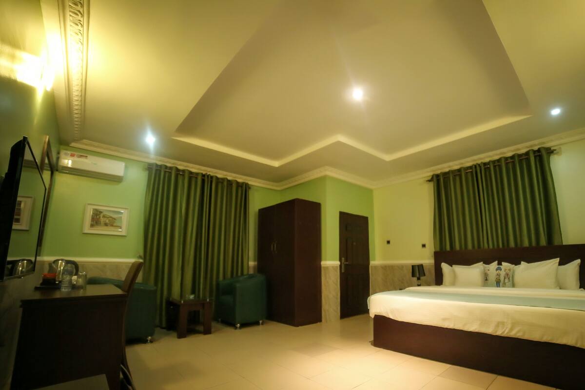 Een hotelkamer met een bed, een bureau, een stoel, een kledingkast en een groen gordijn.