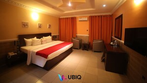 A hotel room with a large bed, a desk, a chair, a TV, and an air conditioning unit. - Ubiq Suites and Apartments (Abuja)