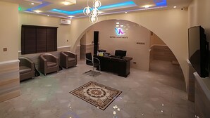 A hotel reception area with a desk, chairs, a TV, and a patterned rug. - Ubiq Suites and Apartments (Abuja)