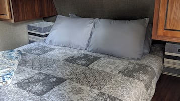 A bed with a patterned bedspread and a single pillow, a wooden nightstand, and a drawer unit with a handle.