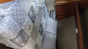 Una cama con una colcha estampada y una sola almohada, una mesita de noche de madera y un mueble con cajones y un tirador.