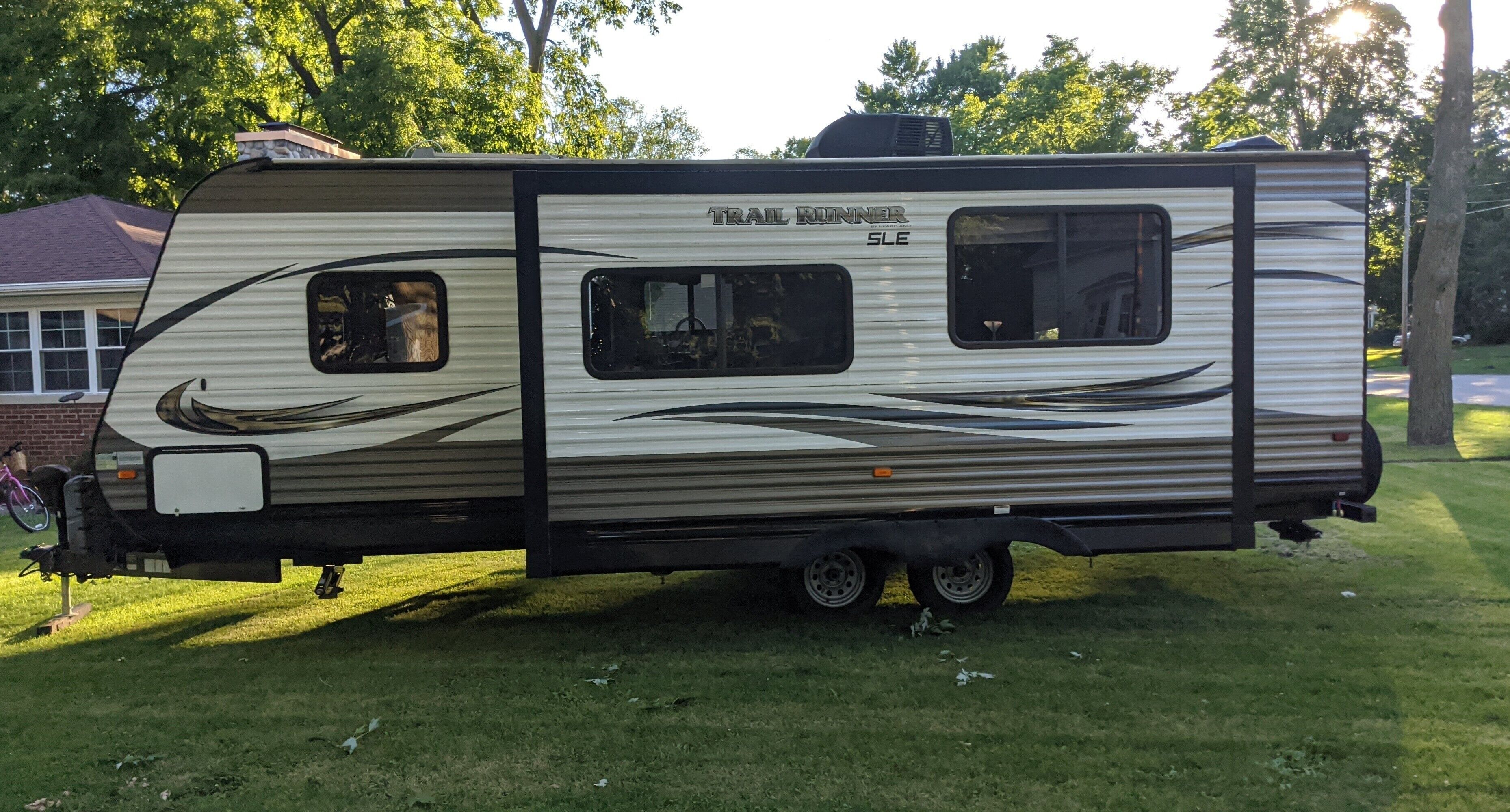 Un camping-car de la marque Trail Runner SLE est stationné sur une pelouse, avec une maison en briques en arrière-plan.