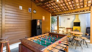 A foosball table in a wooden-floored room with a tiled ceiling, a black refrigerator, and a yellow stove. - Chalés Mar Virado (Ubatuba)