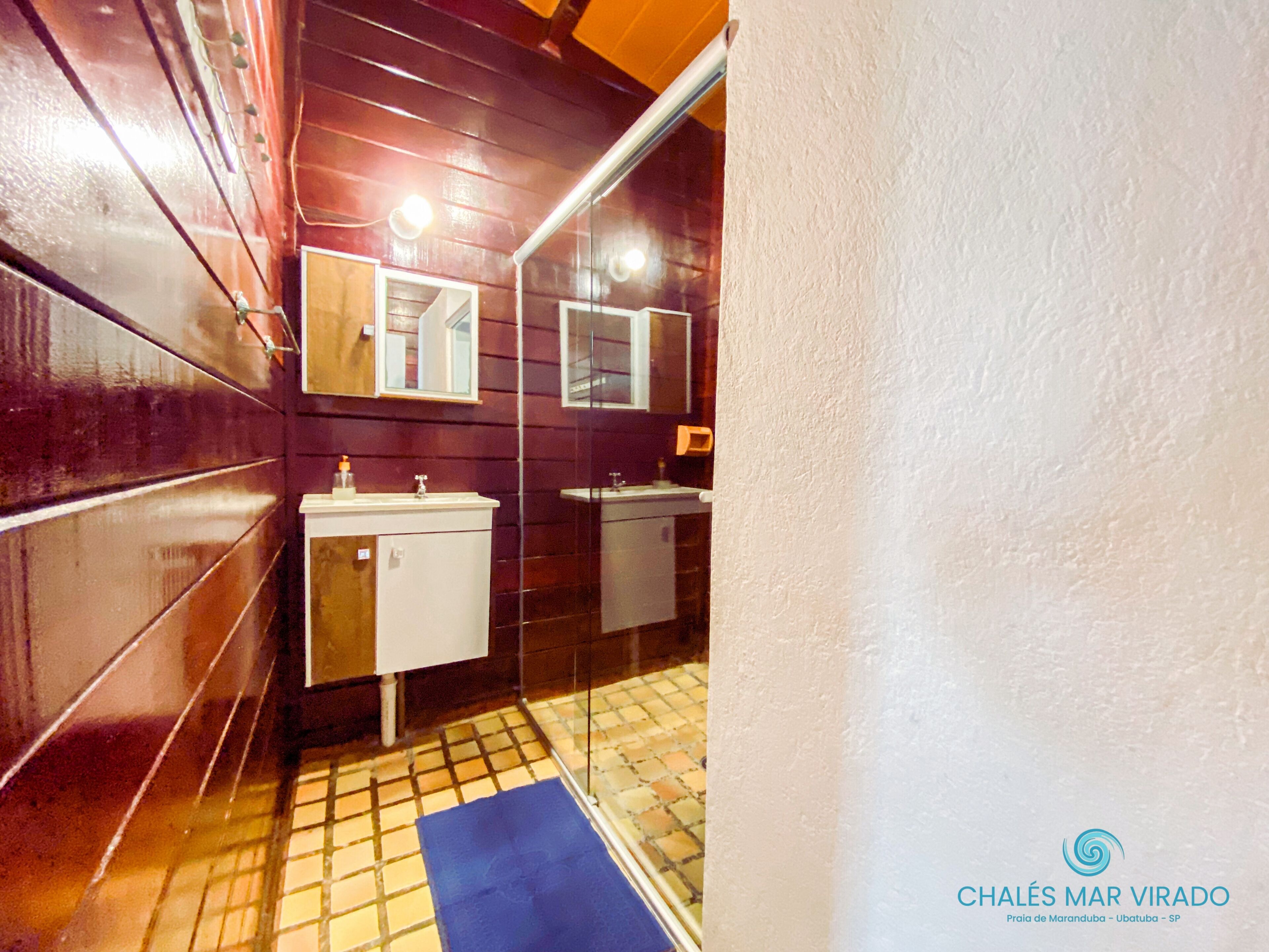 A narrow bathroom with wooden walls, two sinks, and a blue mat on the floor.