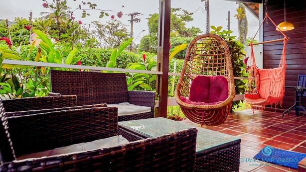 A covered outdoor seating area with wicker furniture and a hanging chair. - Chalés Mar Virado (Ubatuba)