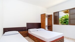 A room with two beds, a brick accent wall, and a window with a view of greenery. - Chalés Mar Virado (Ubatuba)