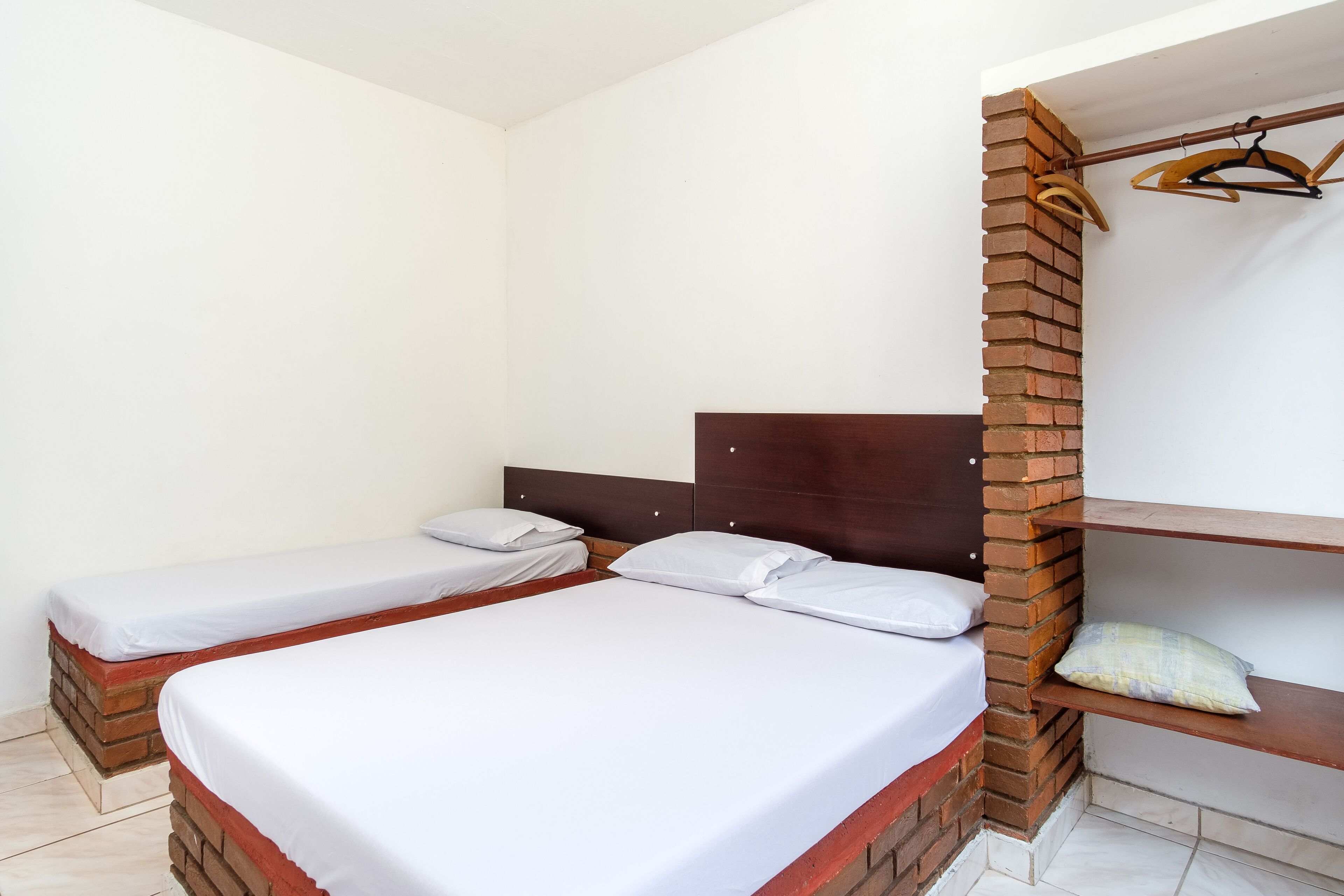 A room with two beds, a brick wall, and a wooden headboard.