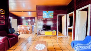 A cozy living area with a wooden ceiling, a dining table with chairs, a TV, and a blue sofa. - Chalés Mar Virado (Ubatuba)