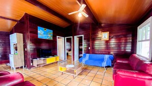 A cozy living room with a red sofa, a television, and a coffee table. There is a ceiling fan and a painting on the wall. - Chalés Mar Virado (Ubatuba)