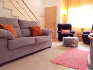 Una sala de estar con un sofá gris, un otomaní y dos sillones.
