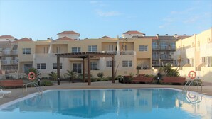 Une piscine dotée d’une pergola, entourée d’immeubles à plusieurs étages avec des balcons et un poste de surveillance pour les sauveteurs.