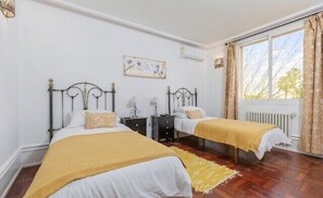 A bedroom with two beds, a window with curtains, a radiator, and a painting on the wall. - Large Luxury  Villa , with Large Gardens , pool ,gym and tennis court. (santa pola)