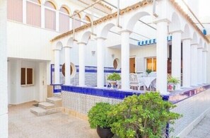 A courtyard with white columns, blue-tiled steps, and a dining area with tables and chairs. - Large Luxury  Villa , with Large Gardens , pool ,gym and tennis court. (santa pola)