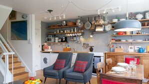 Una cocina moderna con estantes de madera, un comedor con una silla tapizada en rojo, y un frutero sobre una mesa de madera.