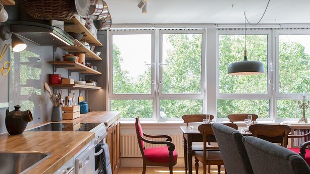 Una cocina moderna con armarios de madera, un ventanal grande y una zona de comedor con sillas y una mesa.