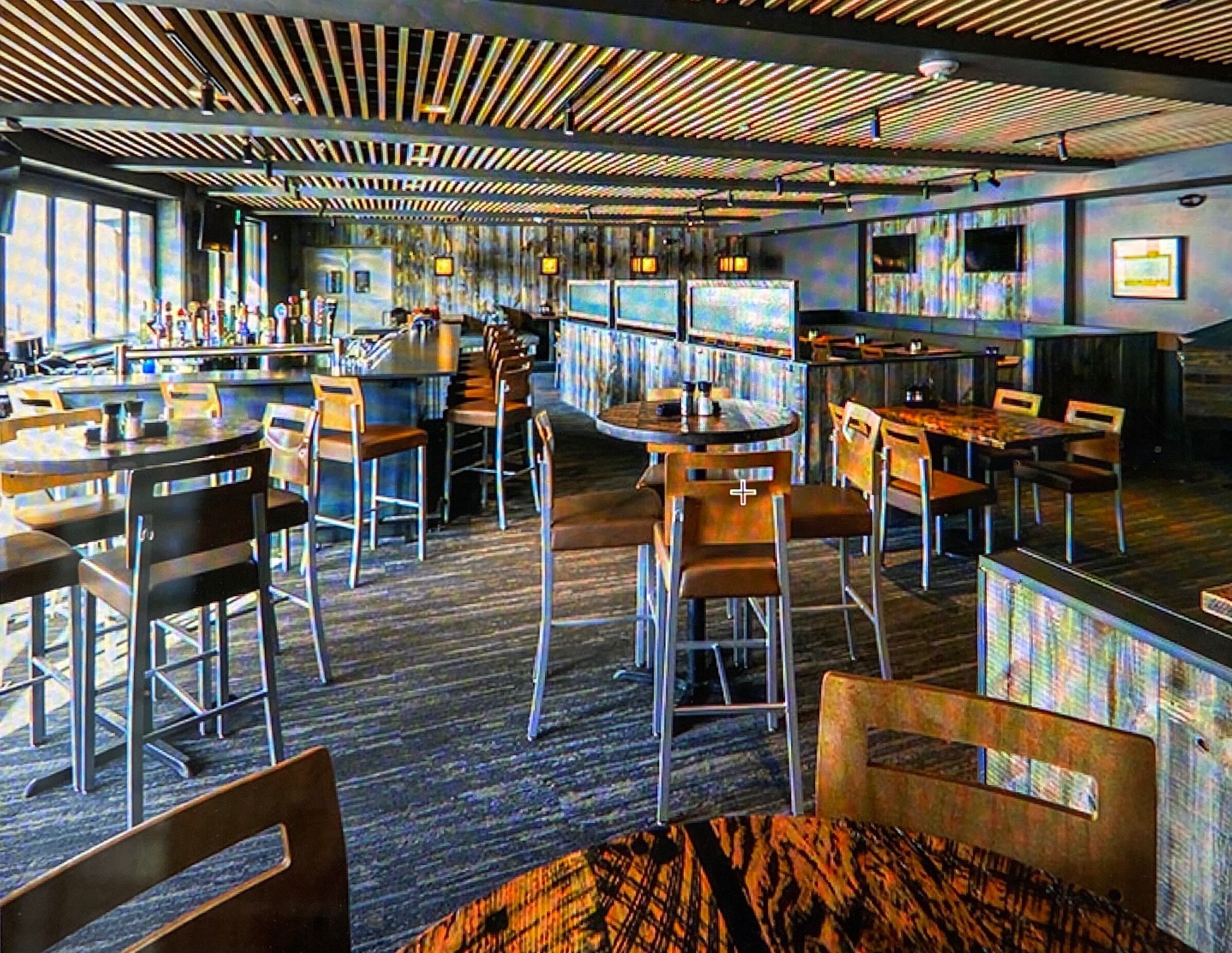 Un restaurante moderno con suelo de madera, varias zonas de estar y una barra con un diseño de techo original.