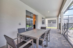 An outdoor patio with a wooden table and chairs, a glass door leading to an interior space, and a view of the sky.