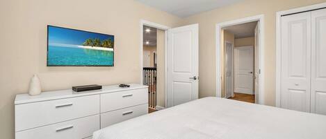 Un dormitorio con cama, cómoda, televisor en la pared y puerta que da a otra habitación.