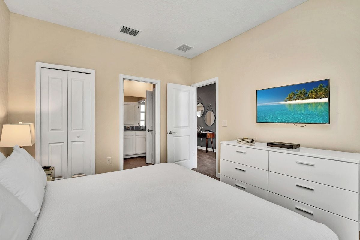 A bedroom with a bed, a dresser, a television, and a painting of a beach scene.