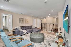 A spacious living area with a sectional sofa, ottoman, and a glass coffee table.