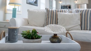 A modern living room with a white sofa, striped pillows, a small potted plant, a candle, and a decorative vase on a tray. - Classic Beach Cottage on Oceanside of Wrightsville Beach-Upper Unit (Wrightsville Beach)