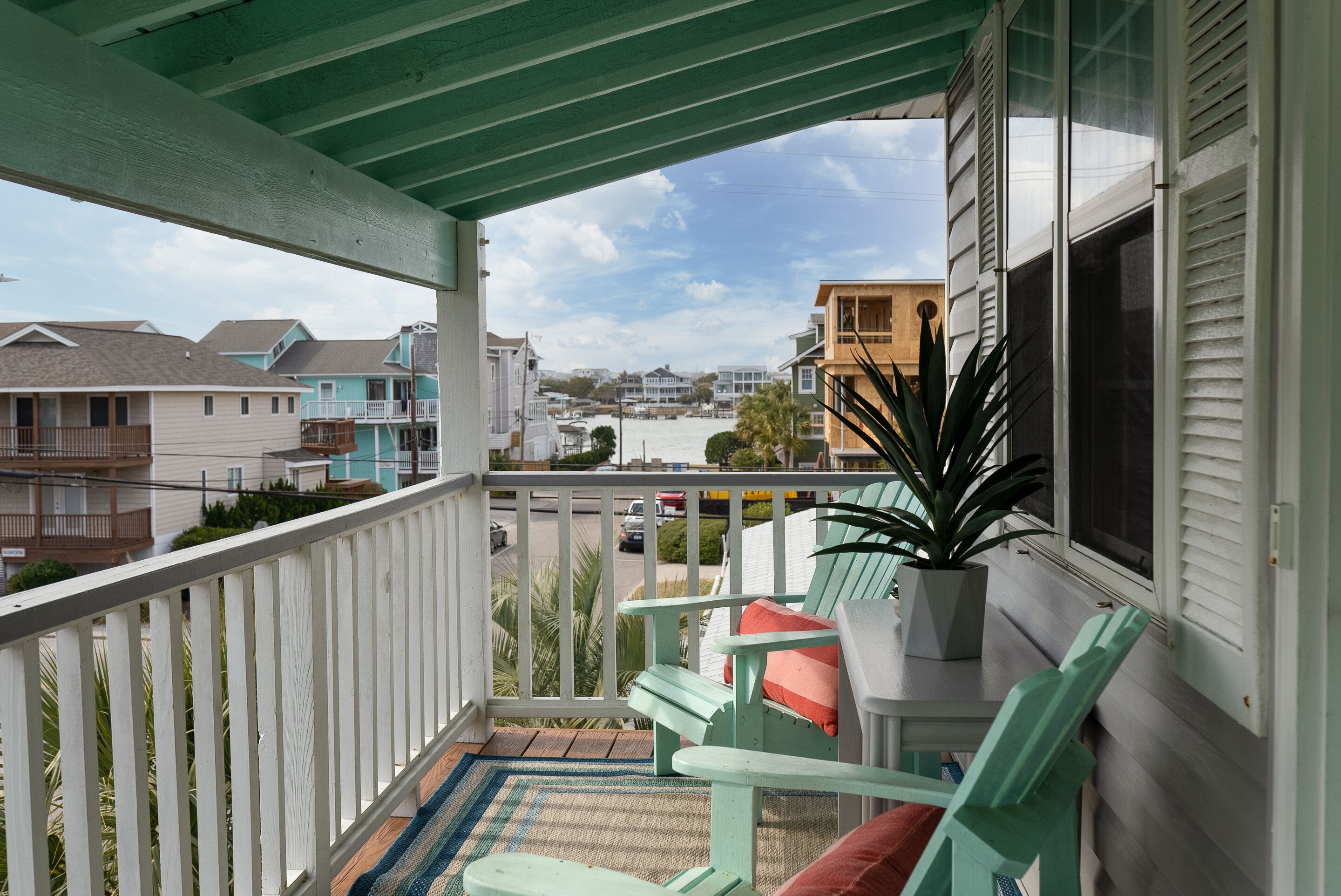 A balcony with a view of a residential area, a potted plant, and two green chairs with cushions.