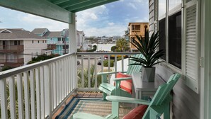 A balcony with a view of a residential area, a potted plant, and two green chairs with cushions. - Classic Beach Cottage on Oceanside of Wrightsville Beach-Upper Unit (Wrightsville Beach)