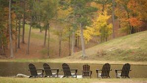 A row of Adirondack chairs by a lake with autumn foliage in the background. - Mtn Cabin Lake Hot Tub | Kayak | Fish | AtvTrls (MENA)
