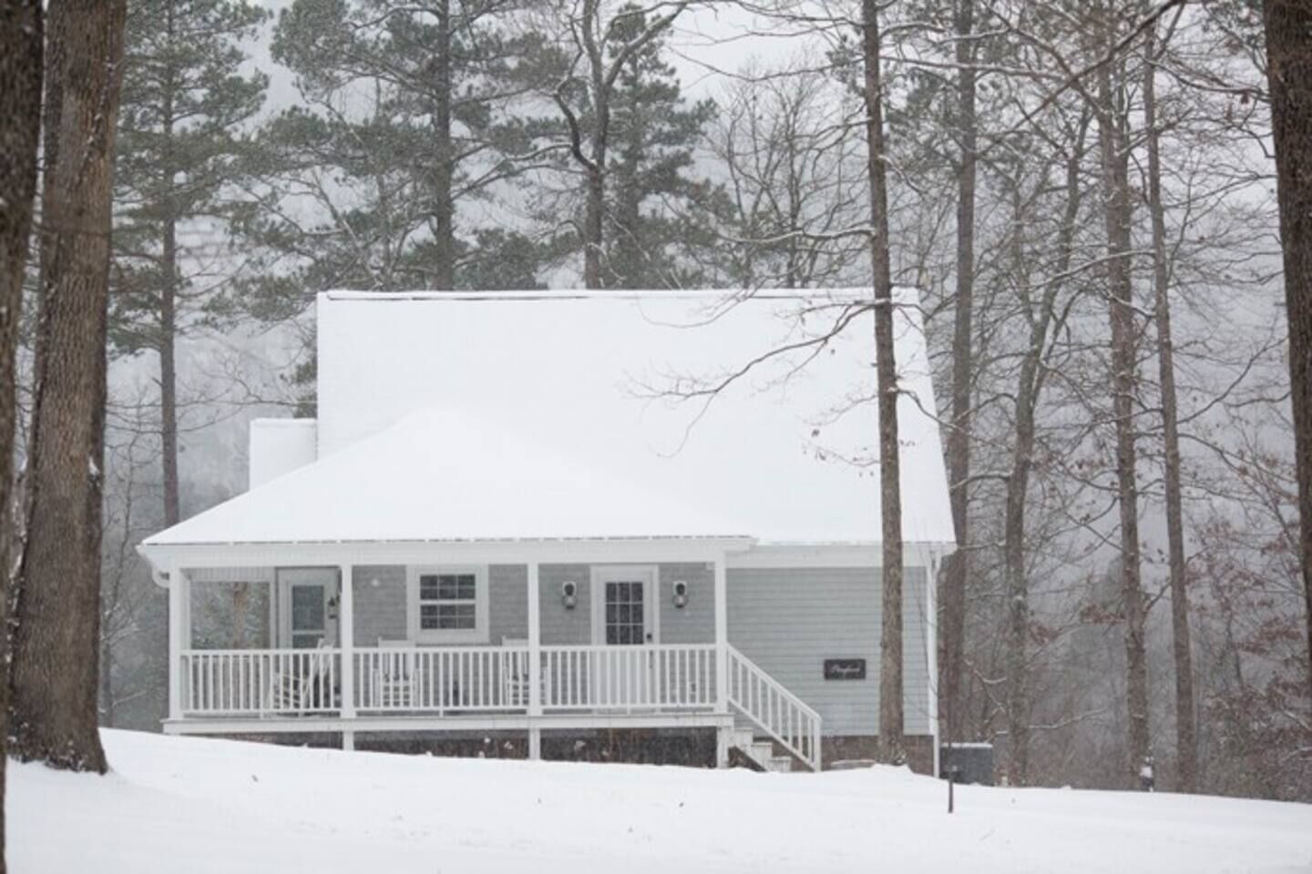 Een huis bedekt met sneeuw, met een veranda en schoorsteen, omringd door bomen.