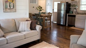A living room with a beige sofa, a wooden dining table, and a kitchen area with a refrigerator and cabinets. - Mtn Cabin Lake Hot Tub | Kayak | Fish | AtvTrls (MENA)