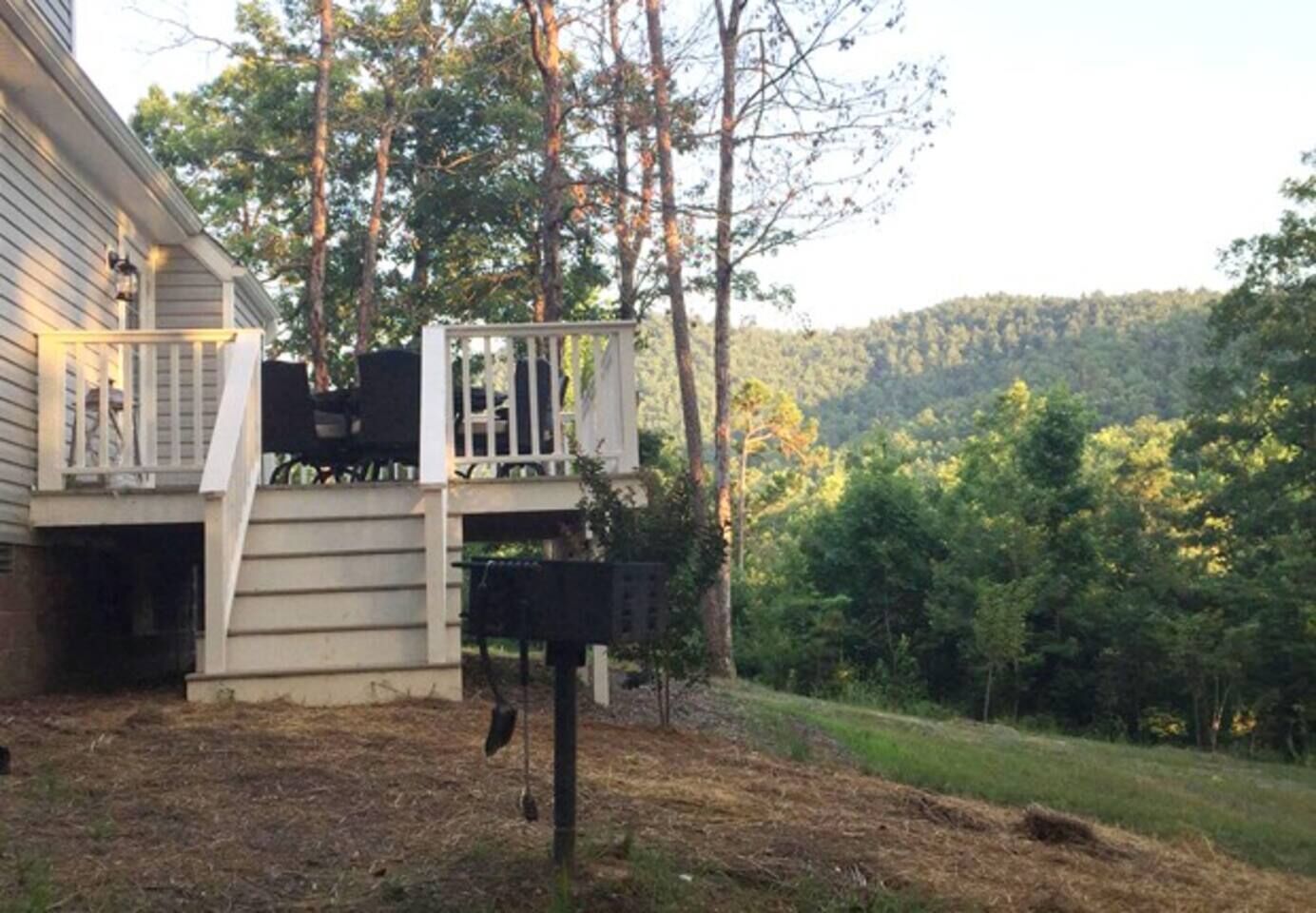 A house with a deck, a bird feeder, and a forested hillside in the background.