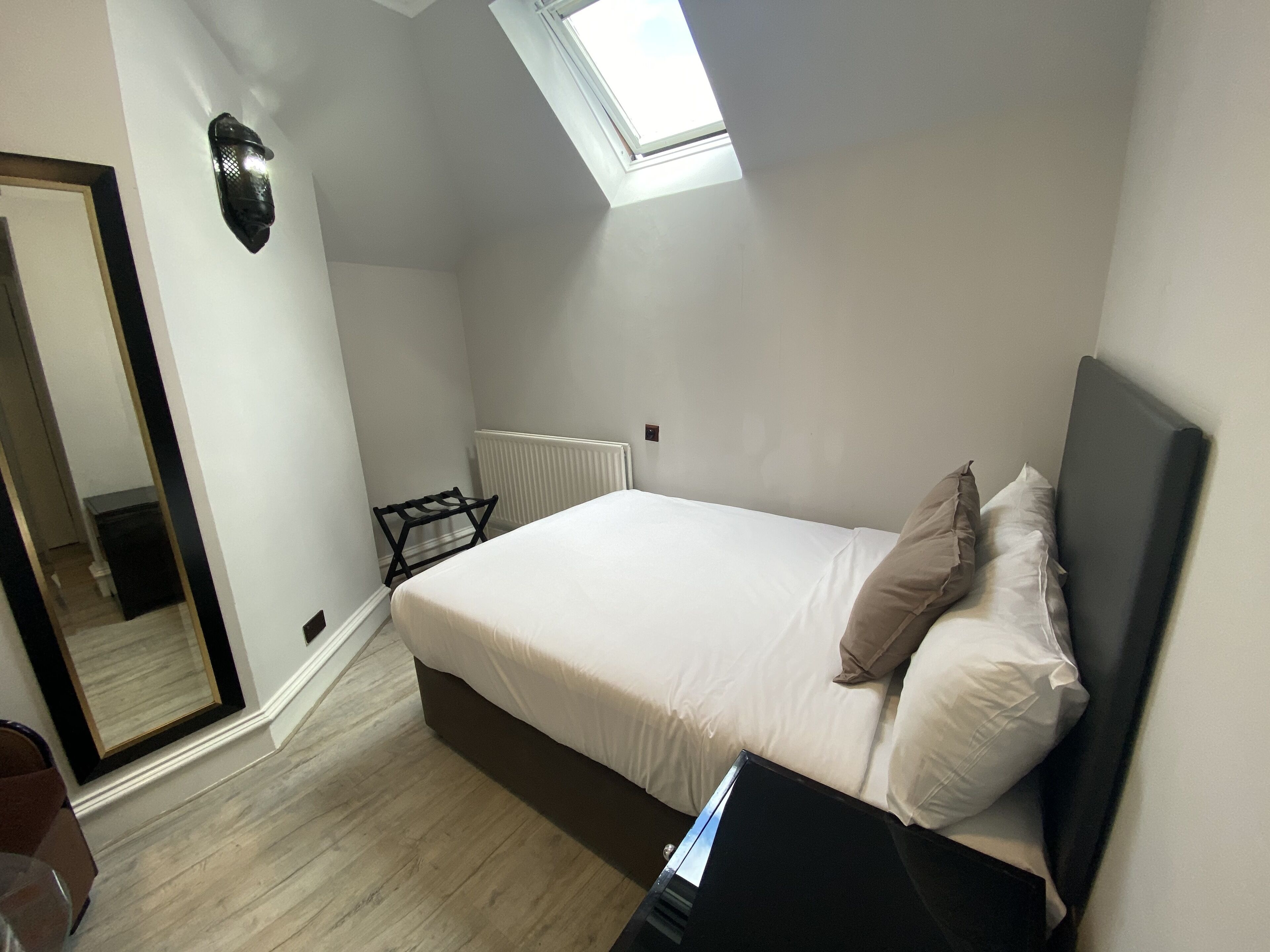 A bedroom with a bed, a black nightstand, a window, and a radiator.