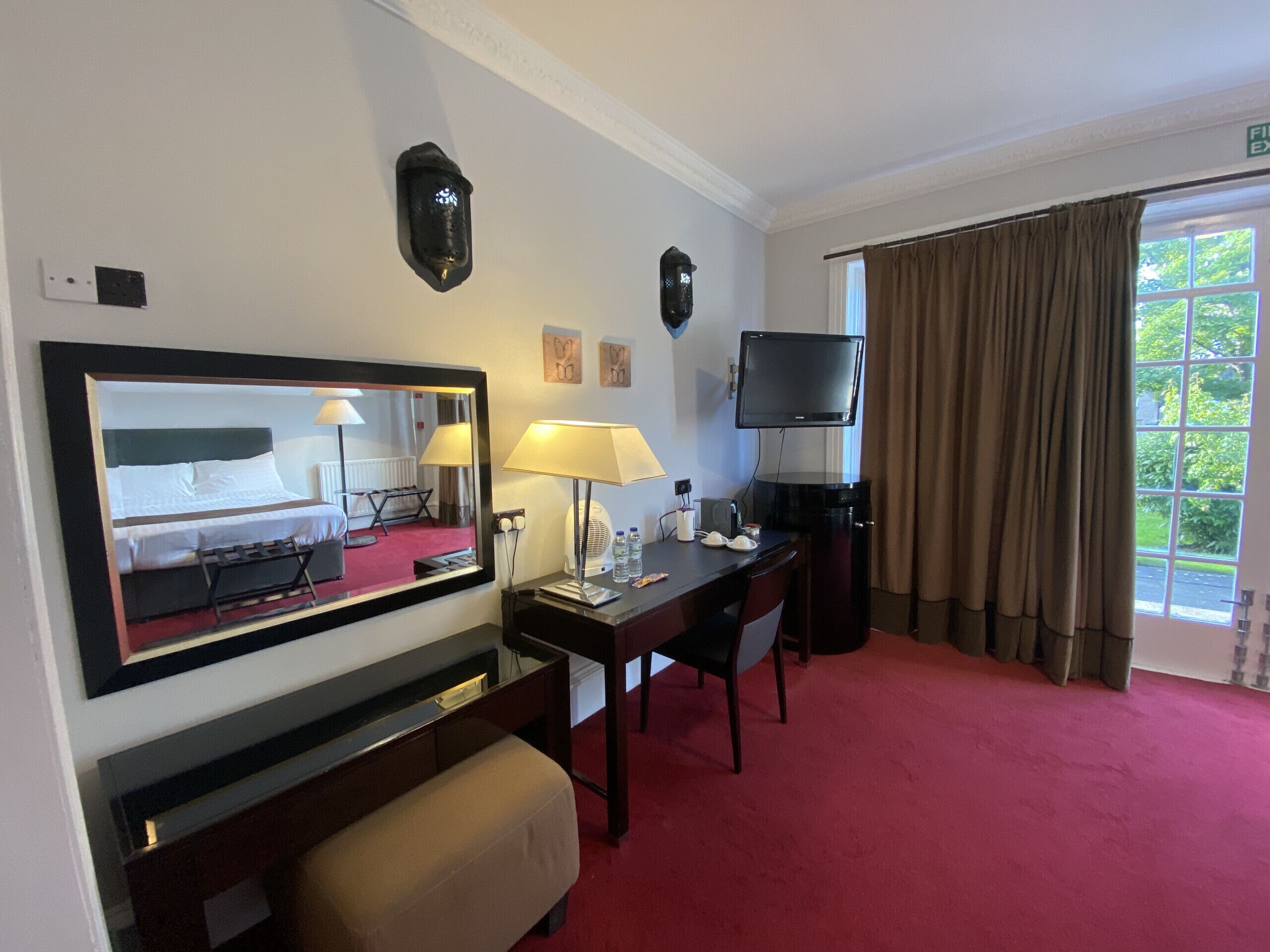Une chambre d’hôtel équipée d’un lit, d’un bureau, d’une chaise, d’une télévision, d’une lampe et d’un grand miroir.